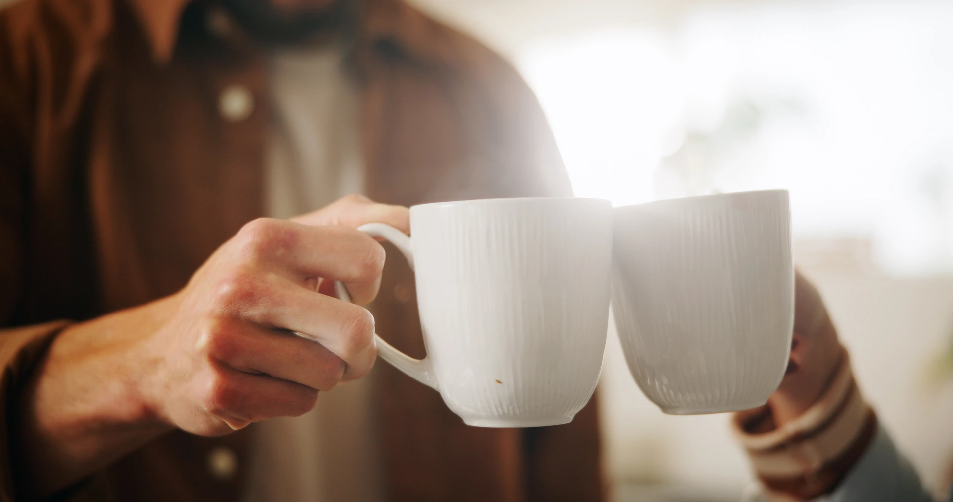 Två händer håller vita kaffemuggar och skålar mot varandra.
